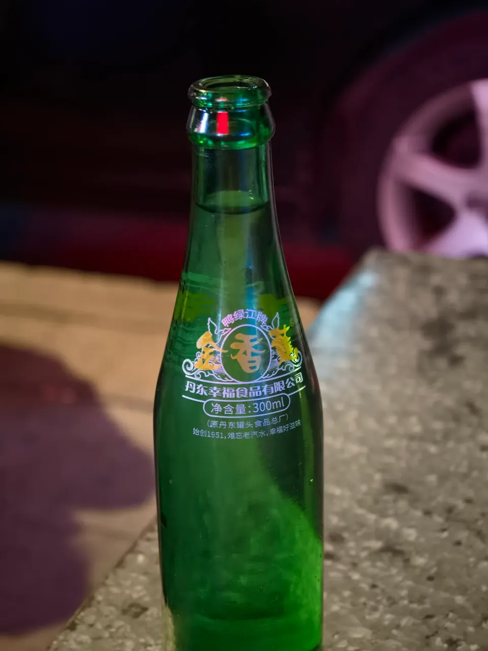 A green glass soda bottle on an outdoor dining table.