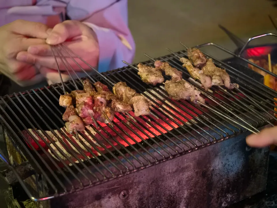 Meat skewers cooking over a tabletop charcoal grill.