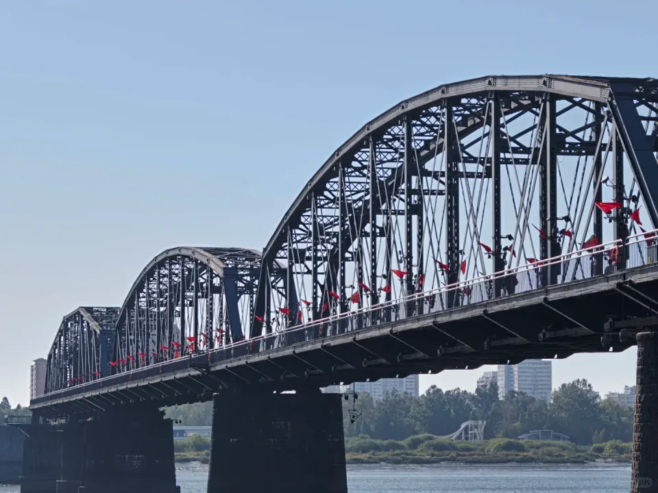 A steel arch bridge lined with flags over the Yalu River.