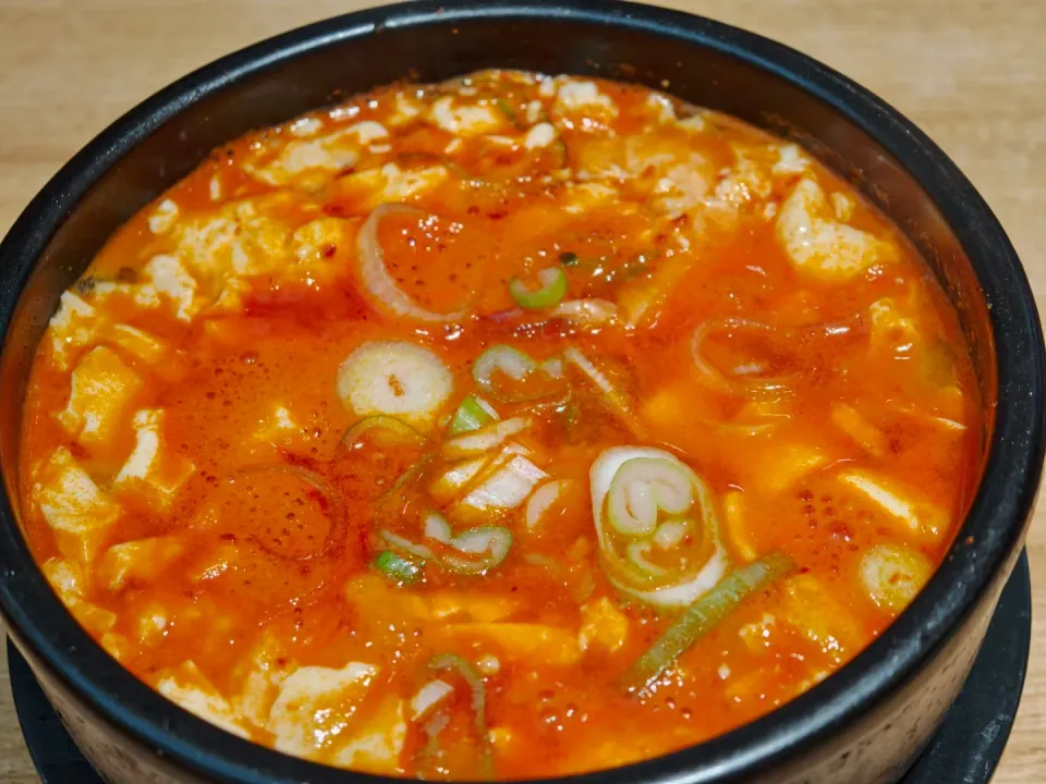 A bubbling red soup topped with sliced scallions.