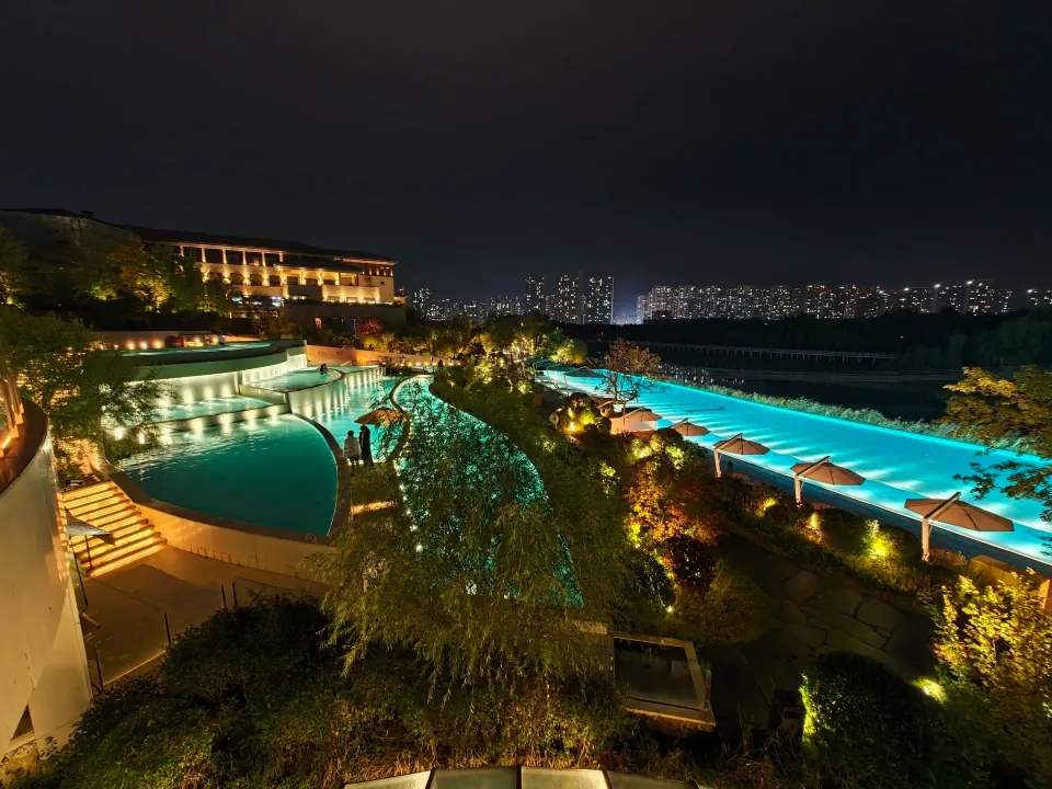 Turquoise outdoor pools glowing beside landscaped paths at night.