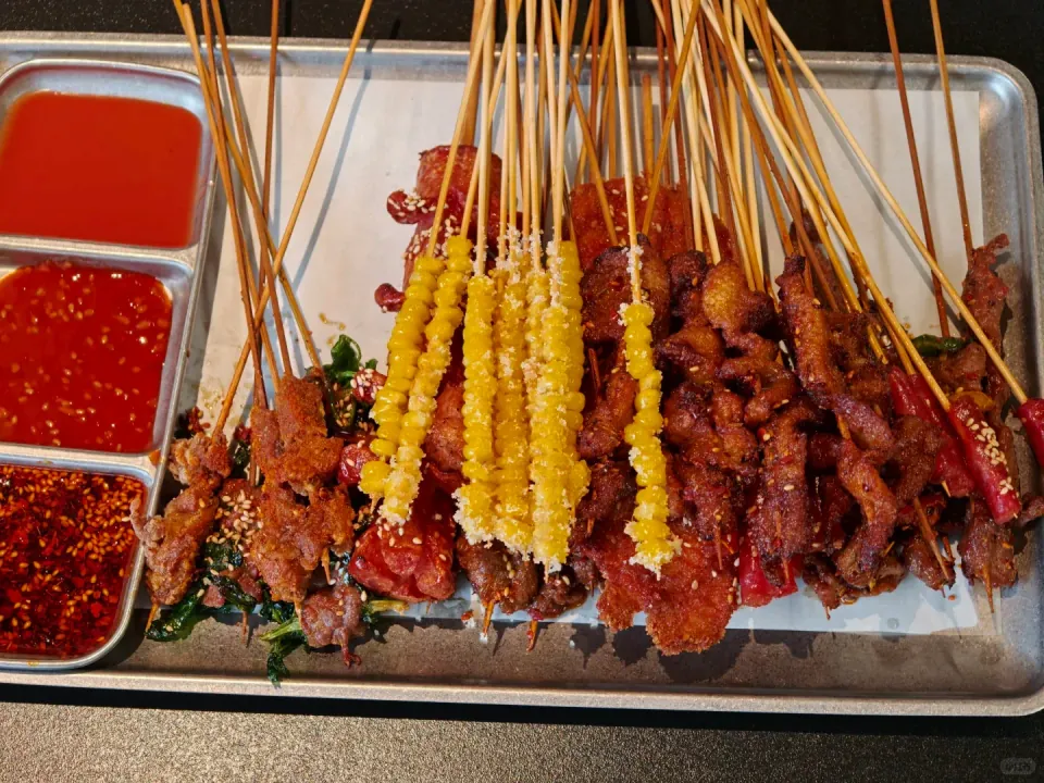 A tray of assorted grilled skewers with dipping sauces.