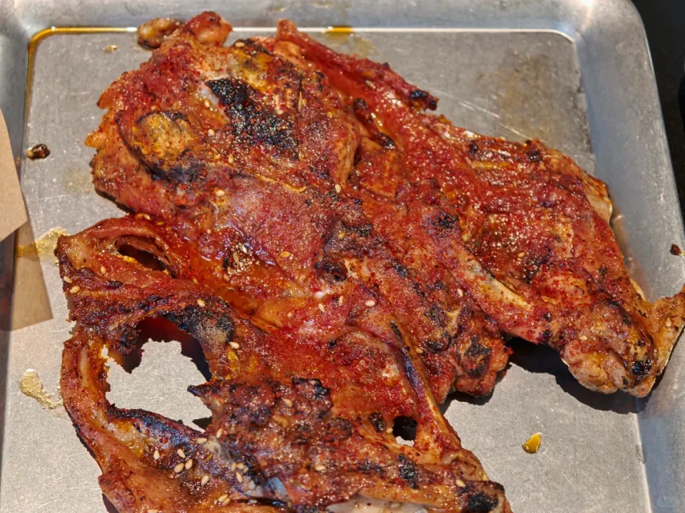 A seasoned grilled chicken frame on a metal tray.