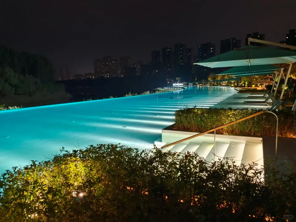 Blue pool water and illuminated steps beside a covered terrace at night.