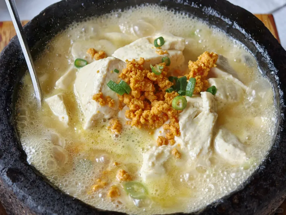 A bubbling pot of tofu topped with scallions and golden crumbs.
