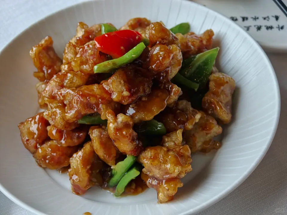 Glazed fried pieces with green and red peppers on a white plate.