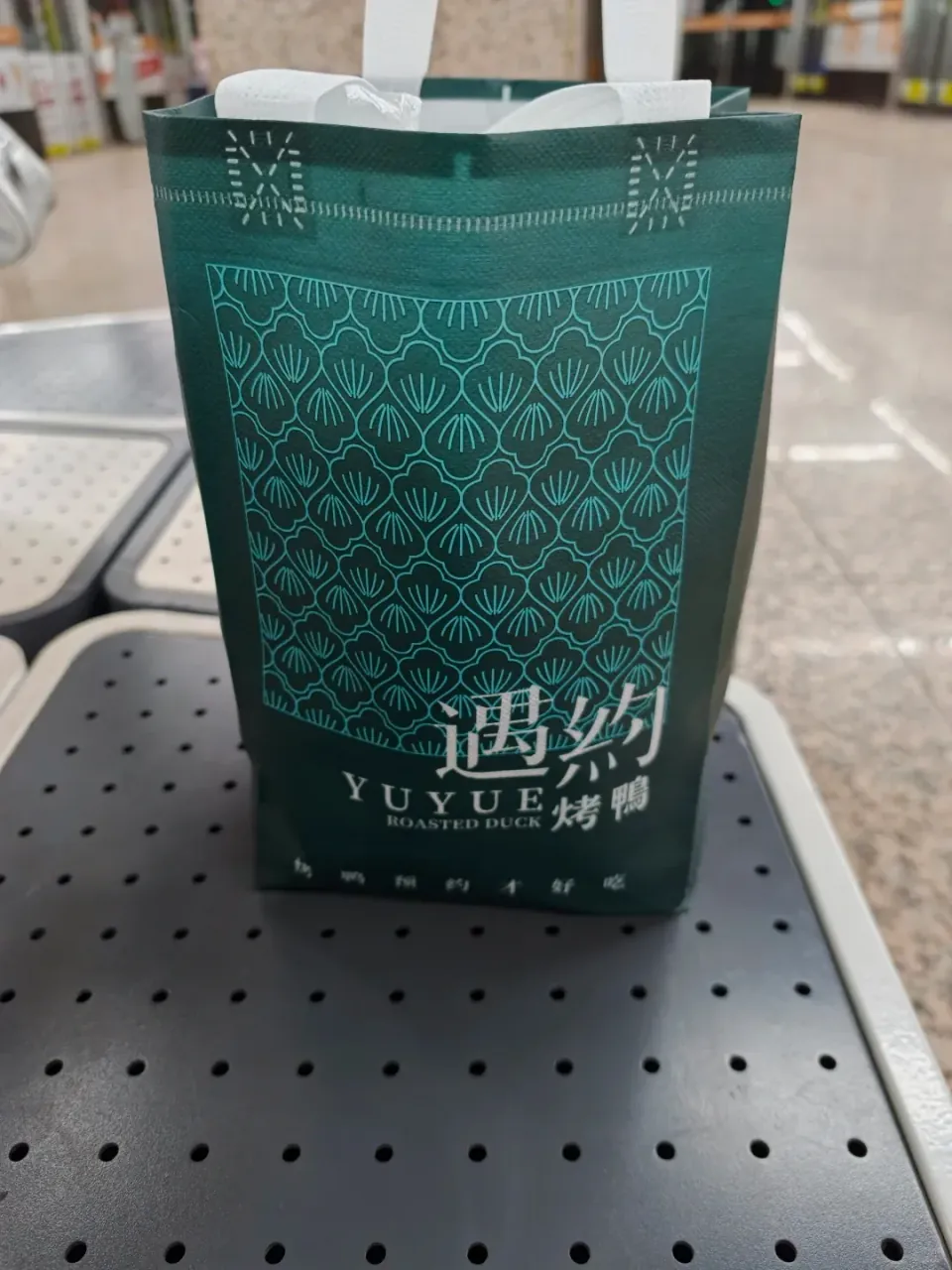 A green patterned shopping bag resting on a metal bench.