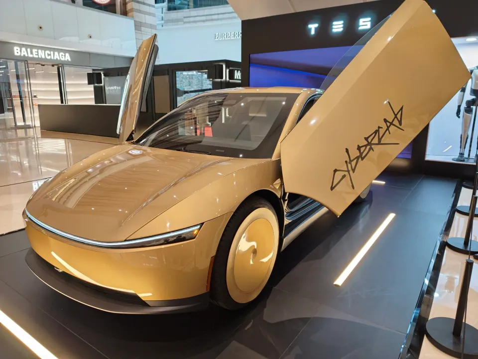 A gold Tesla Cybercab displayed with both doors raised in a shopping mall.