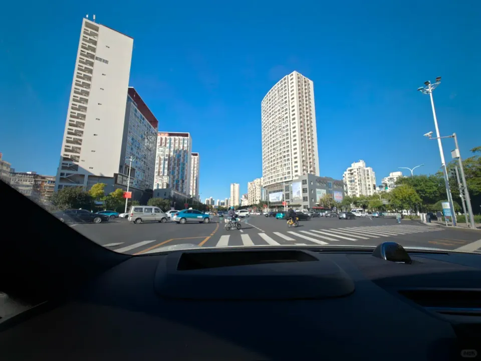 A broad city intersection seen through a car's windshield.