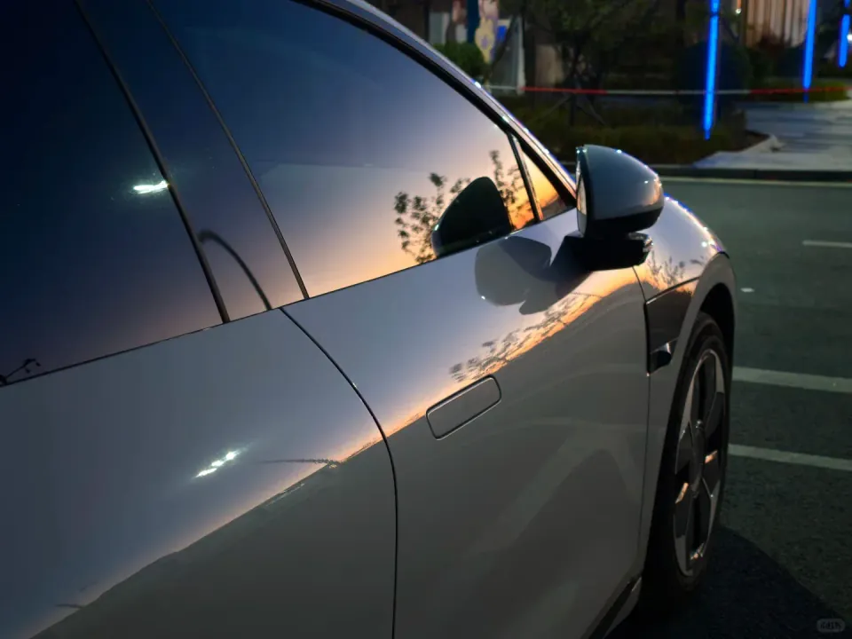 An orange sunset reflected in the windows and body of a white car.