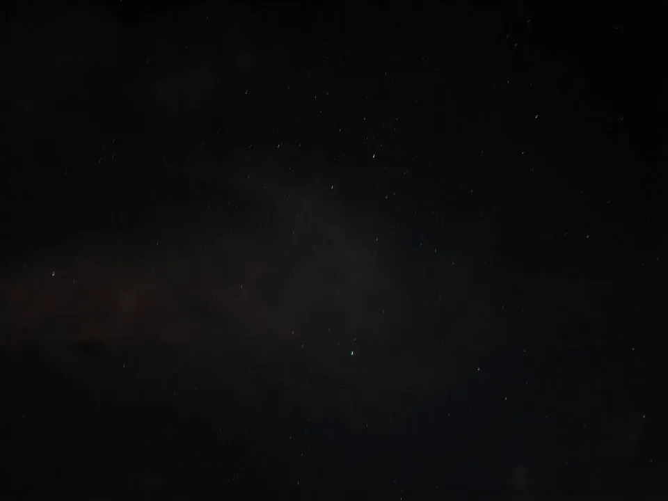 A field of stars above dark clouds in the night sky.